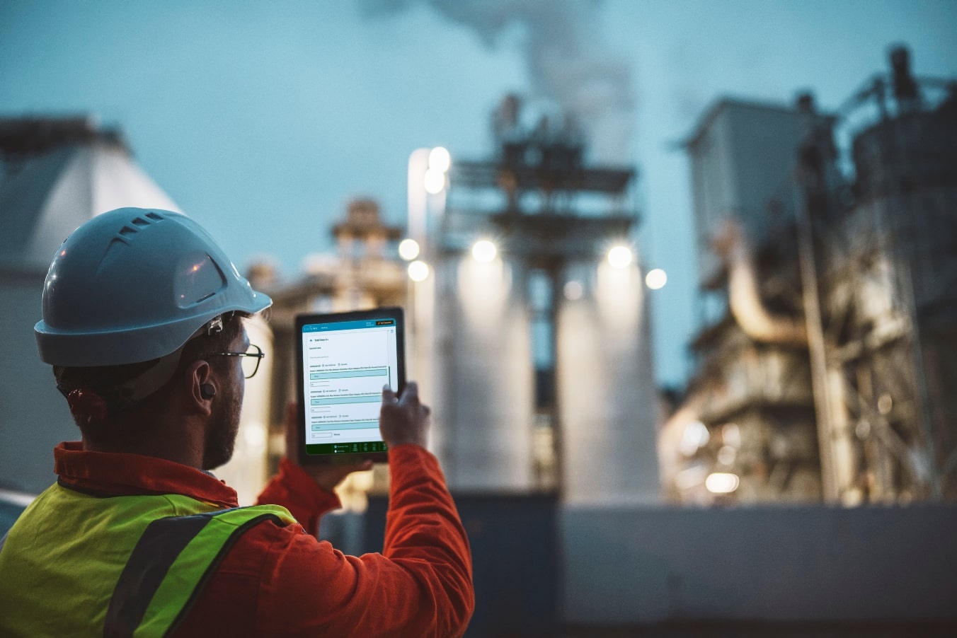 A man with a hard hat reviews STARLIMS Laboratory Execution Systems outside a chemical plant.